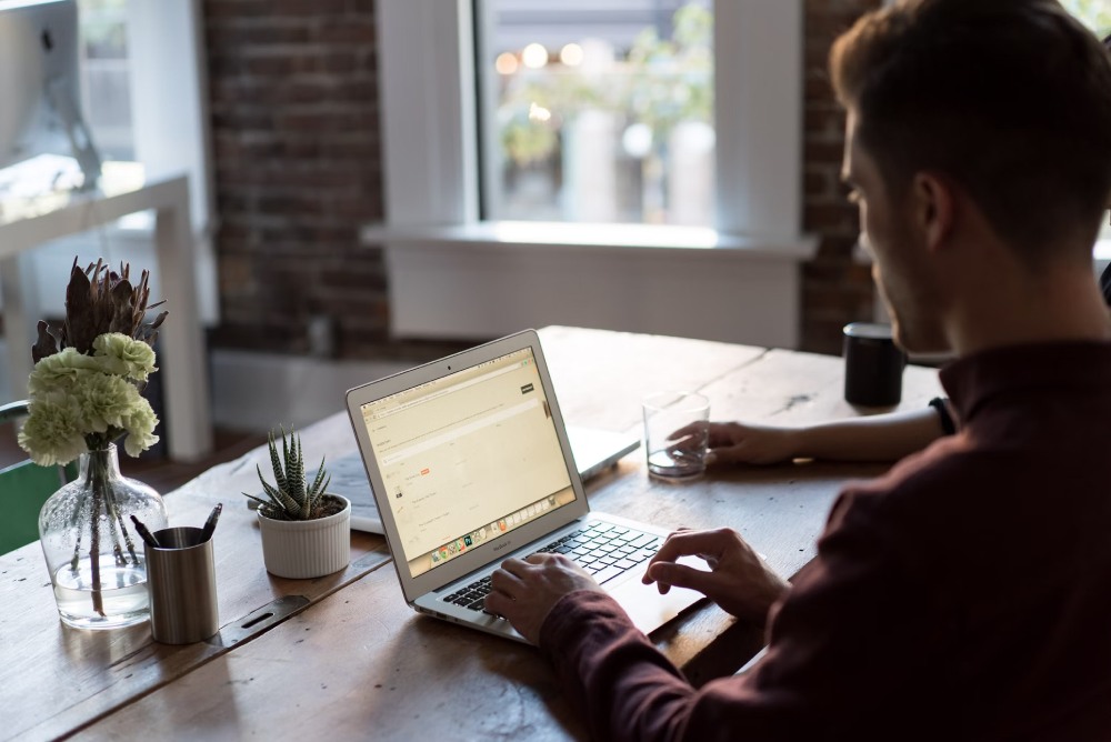 Man sitting at office table with computer and plants.
